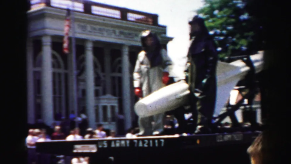 A 1957 Normal, Illinois parade frame shows a rocket or missile on a flatbed passing spectators and storefront architecture.