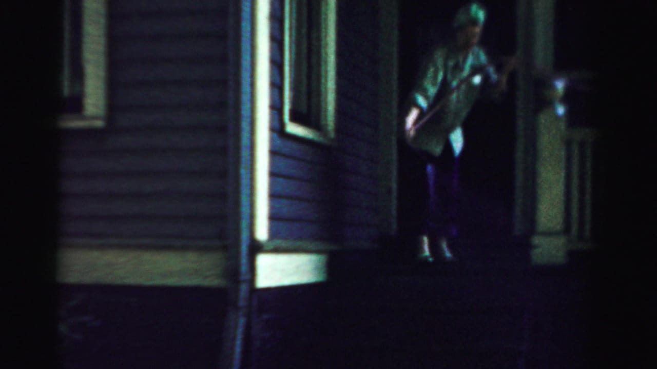 In 1957 Normal, Illinois home-movie footage, an older woman stands near a front entrance under dim night lighting.