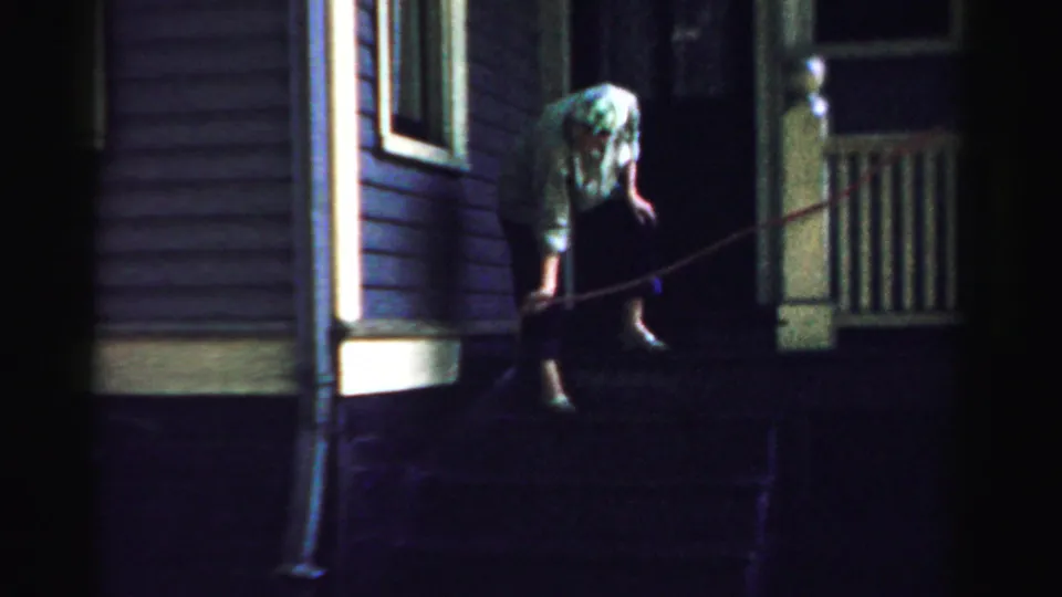 The woman reaches toward the steps while the hose crosses the porch in this 1957 Normal, Illinois night exterior.
