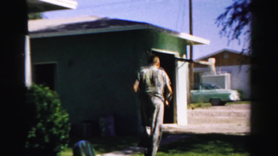 The man walks from the open garage area toward the driveway, with a green house, lawn, and parked car partly visible in Normal, Illinois.