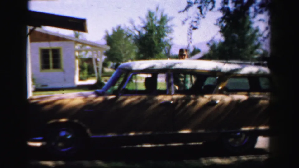 A wood-paneled station wagon sits in shade near a residential lawn and street in 1957 Normal, Illinois home-movie footage.