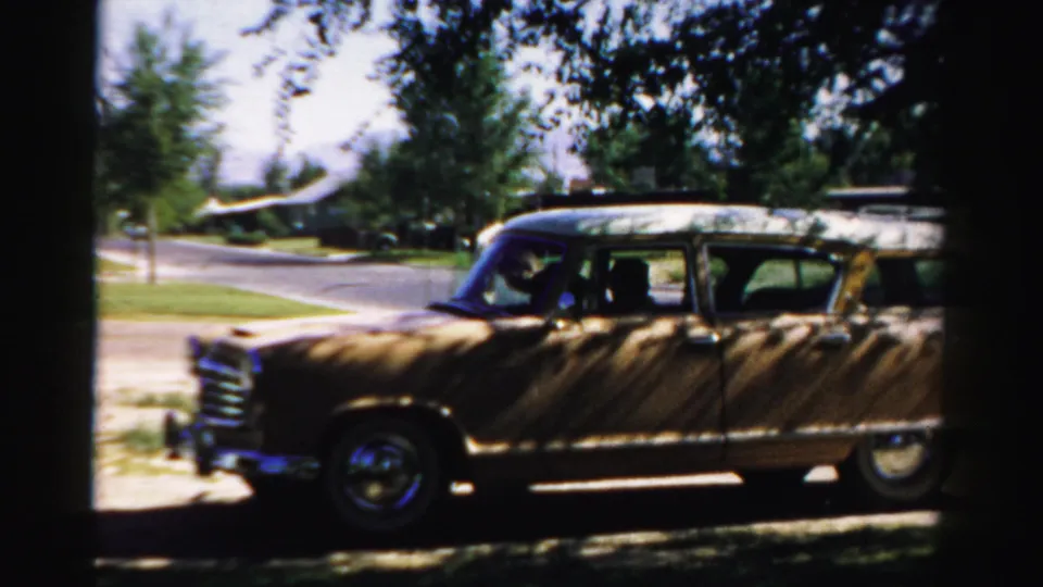 1957 Normal, Illinois frame of a wood-paneled station wagon in side view, with an adult visible inside the front seat area.