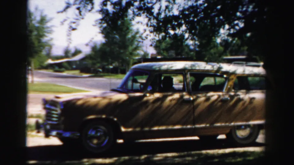1957 Normal, Illinois home-movie frame showing the station wagon under leafy shade, with the suburban street and lawn in the background.