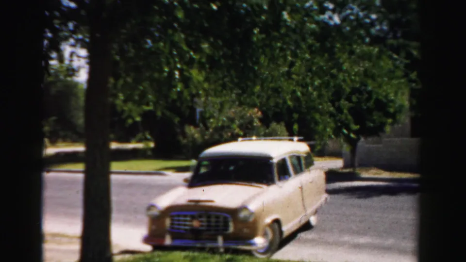 1957 Normal, Illinois home-movie frame showing the wagon front-on near a curb, with trees, lawn, and sidewalk behind it.