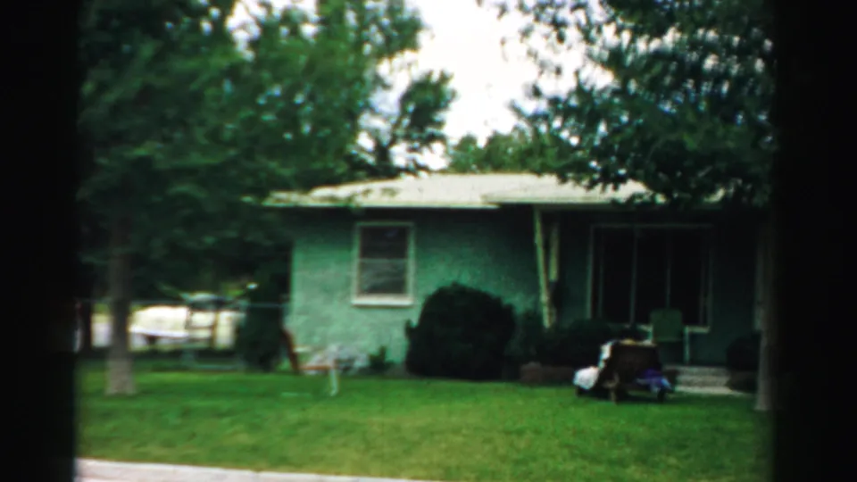 1957 Normal, Illinois home-movie frame showing a green single-story house with a front lawn, shrubs, and trees in daylight.