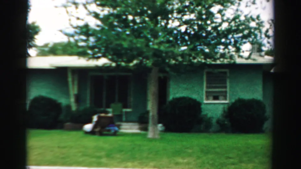The camera holds on the Normal, Illinois house exterior with clipped grass, shrubs, a tree, windows, and porch items visible.