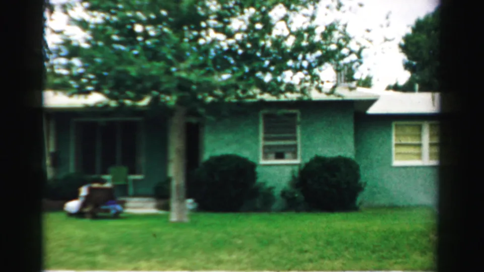 A mid-century residential exterior in Normal, Illinois shows the porch side, lawn, tree, shrubs, and a small toy-like object near the steps.