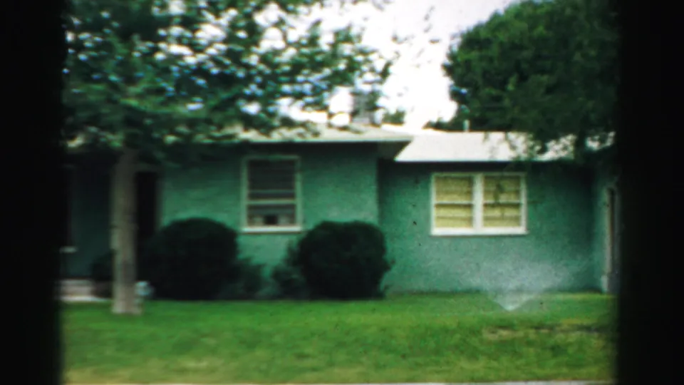 The final frame shows the green house facade in Normal, Illinois with lawn, windows, shrubs, tree branches, and sprinkler water at lower right.