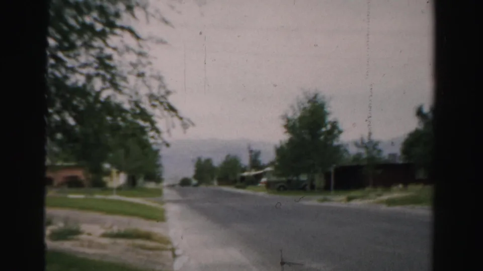 A 1957 home-movie view of a quiet Normal, Illinois street with trees, lawns, and houses in soft focus.