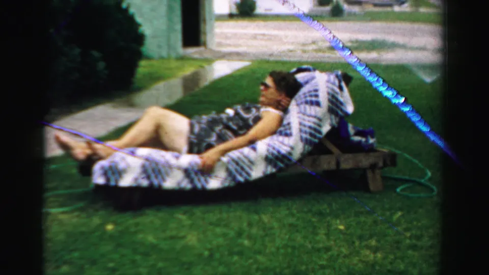 1957 Normal, Illinois home-movie frame showing a woman resting on an outdoor lounge in the yard.