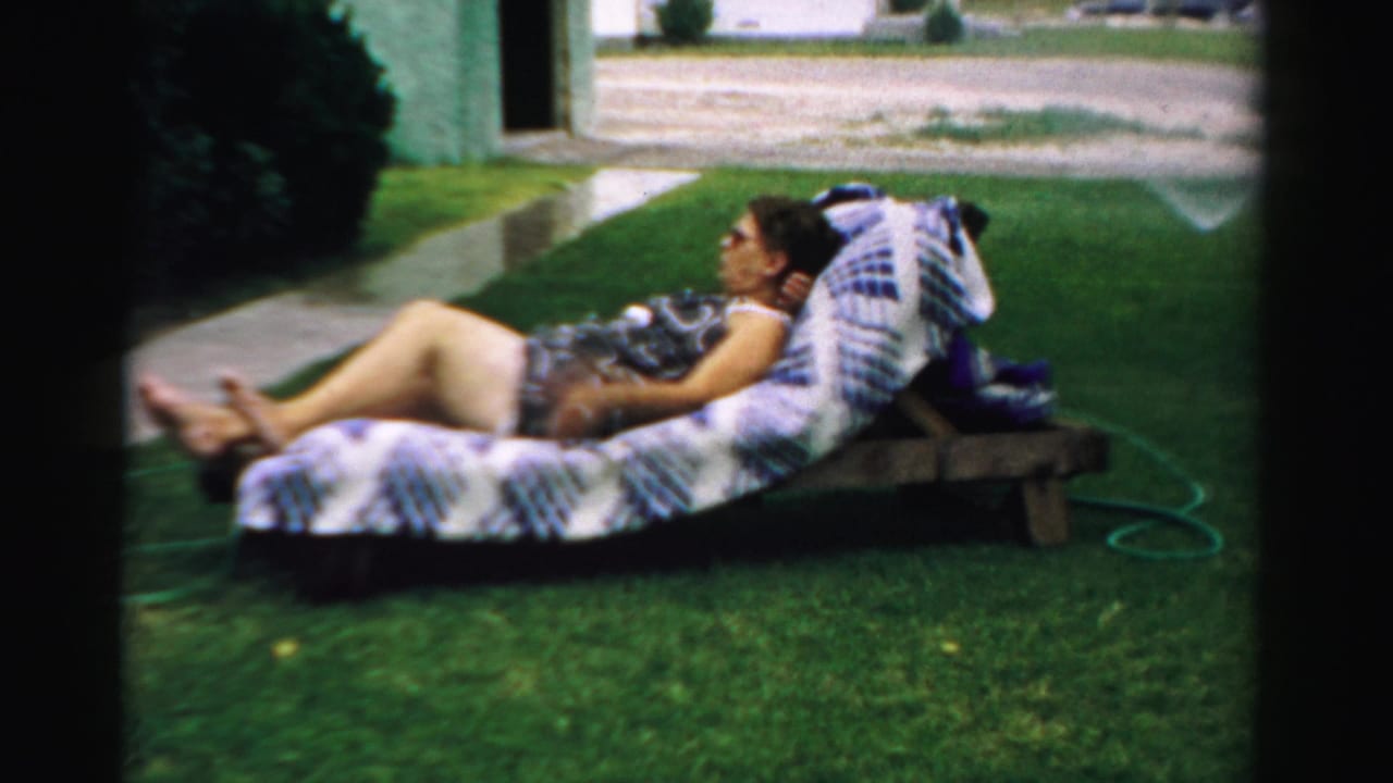 In 1957 Normal, Illinois home-movie footage, a woman reclines on patterned lawn furniture beside a sidewalk and garden hose.