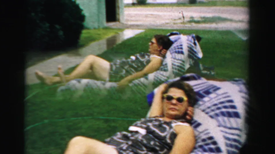 Two women lounge on backyard chairs in Normal, Illinois, with the nearer woman wearing sunglasses and patterned swimwear.