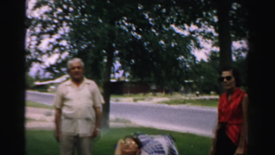 An elderly man in light clothing and a woman in a red top stand near the lawn chair in a suburban Normal, Illinois street scene.