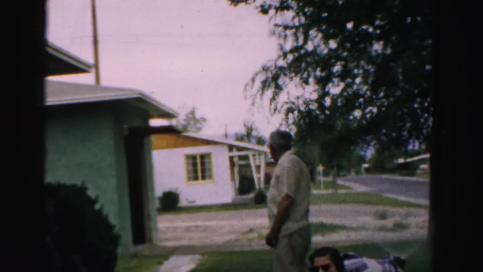 The man turns or walks across the 1957 suburban yard in Normal, Illinois, with the women partly cropped at the lower edge.
