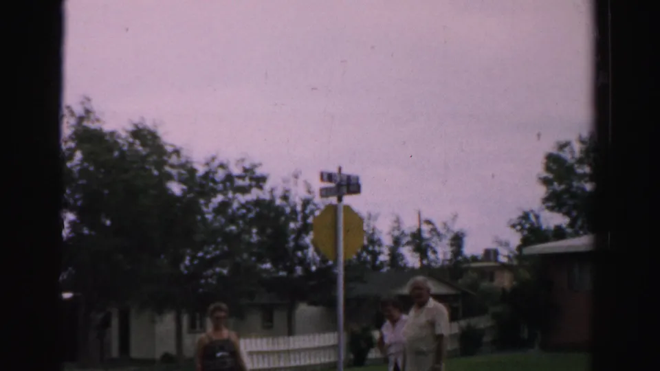 Adults appear near a stop sign at a residential street corner in Normal, Illinois, with a white fence and houses behind them.