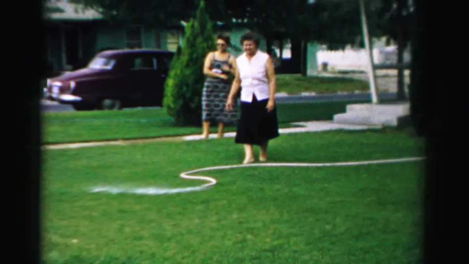 The closing frame shows two women in a 1957 Normal, Illinois yard watching a hose spray across the grass, with a parked car behind them.