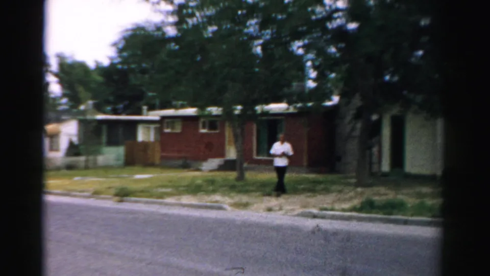 The woman is farther away near the houses in the Normal, Illinois neighborhood, seen across the road in 1957 8mm footage.