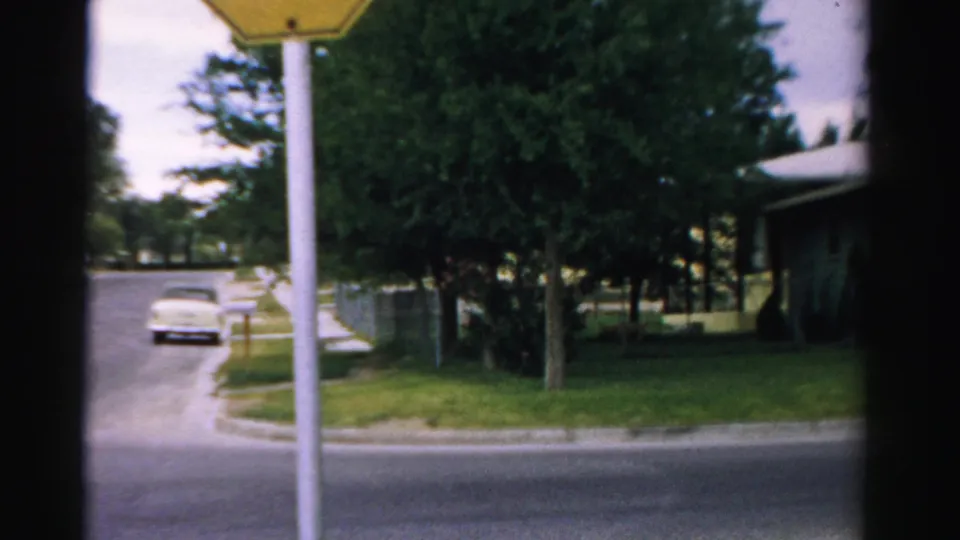 1957 Normal, Illinois street corner with a stop sign, light-colored car, trees, grass, and a residential house.