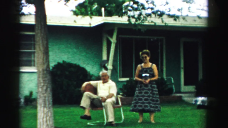 The final frame shows the woman facing the camera on the lawn while the older man remains seated in a folding chair outside the green house.