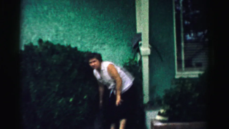 A softly focused 8mm frame shows the woman leaning forward during yard exercise outside a house in Normal, Illinois.