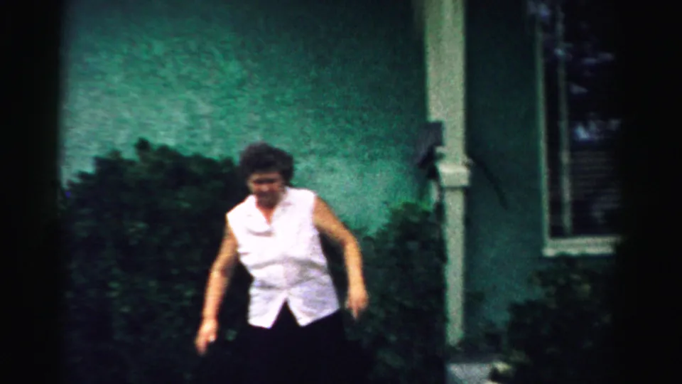 The woman appears mid-motion outside the green house in the 1957 Normal, Illinois home-movie scene.
