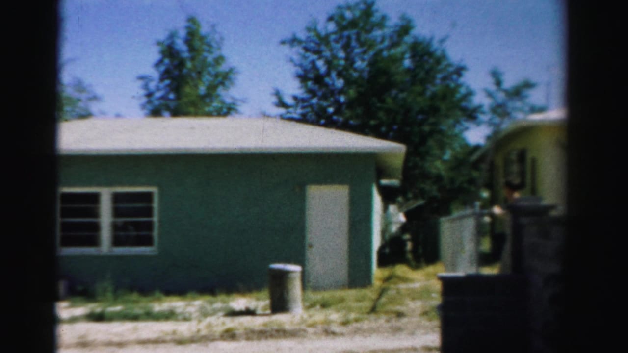 1957 8mm view in Normal, Illinois, showing a greenish-blue residential structure with a white door, windows, yard, and trees.