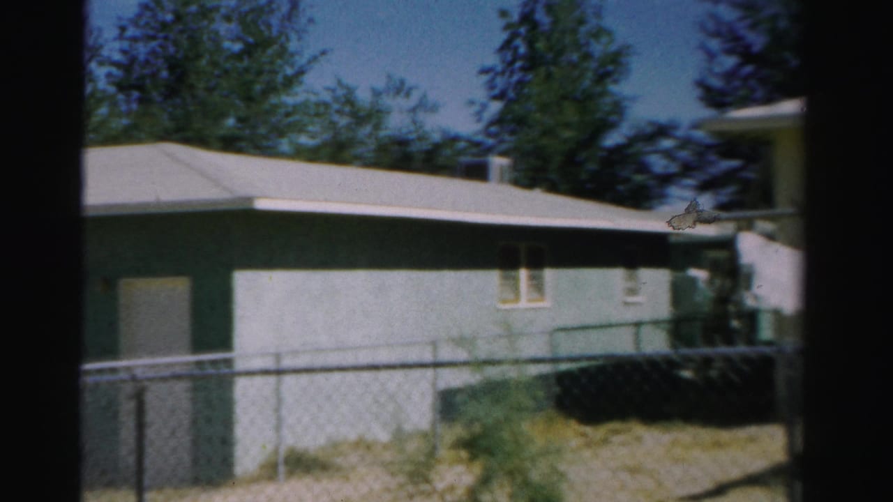 1957 Normal, Illinois home-movie frame showing a single-story house, fence, yard, trees, and blue sky.