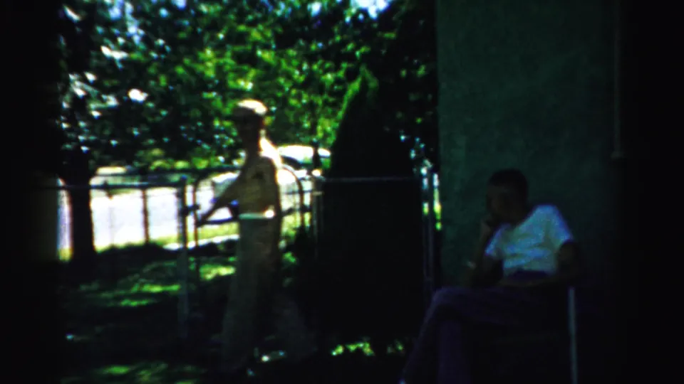 1957 Normal, Illinois yard frame with one man standing near lawn chairs while another adult sits in shade nearby.
