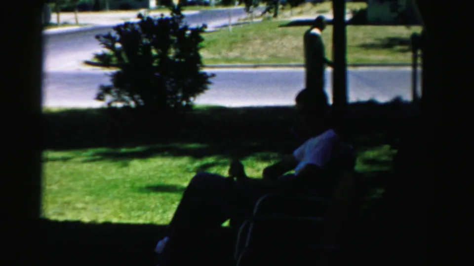 Shaded 1957 Normal, Illinois yard scene with seated adults in silhouette, a lawn, shrub, residential street, and standing figure.