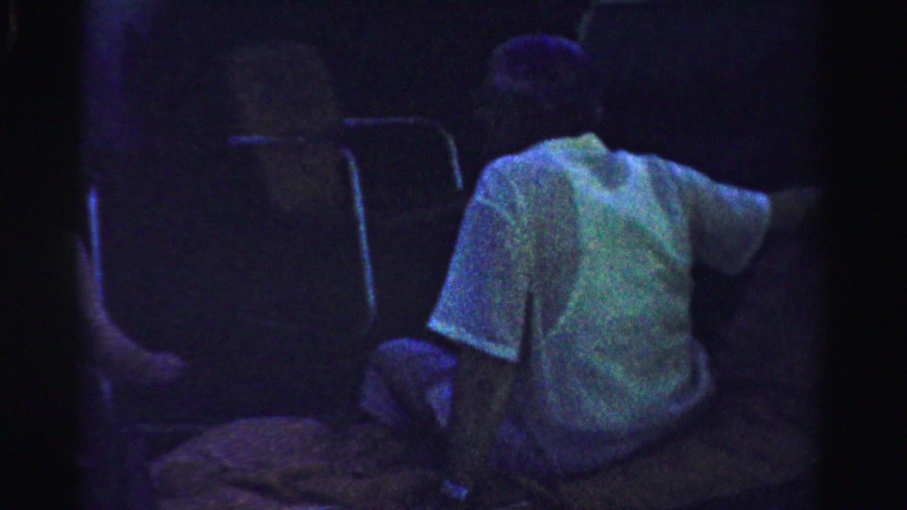Man in a light shirt seated in a dark outdoor area.