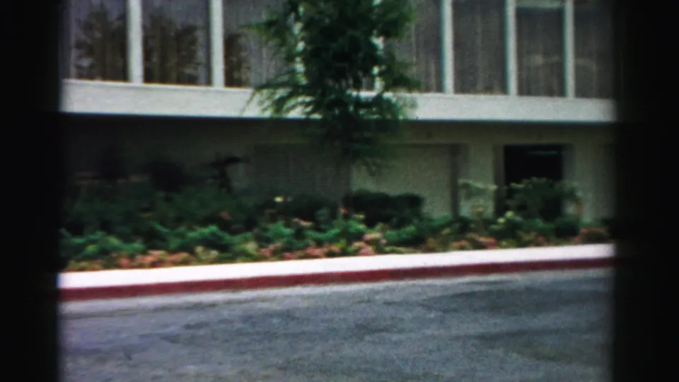 1957 Las Vegas exterior frame with long window bands, low planting beds, a red curb, and asphalt in front of the building.