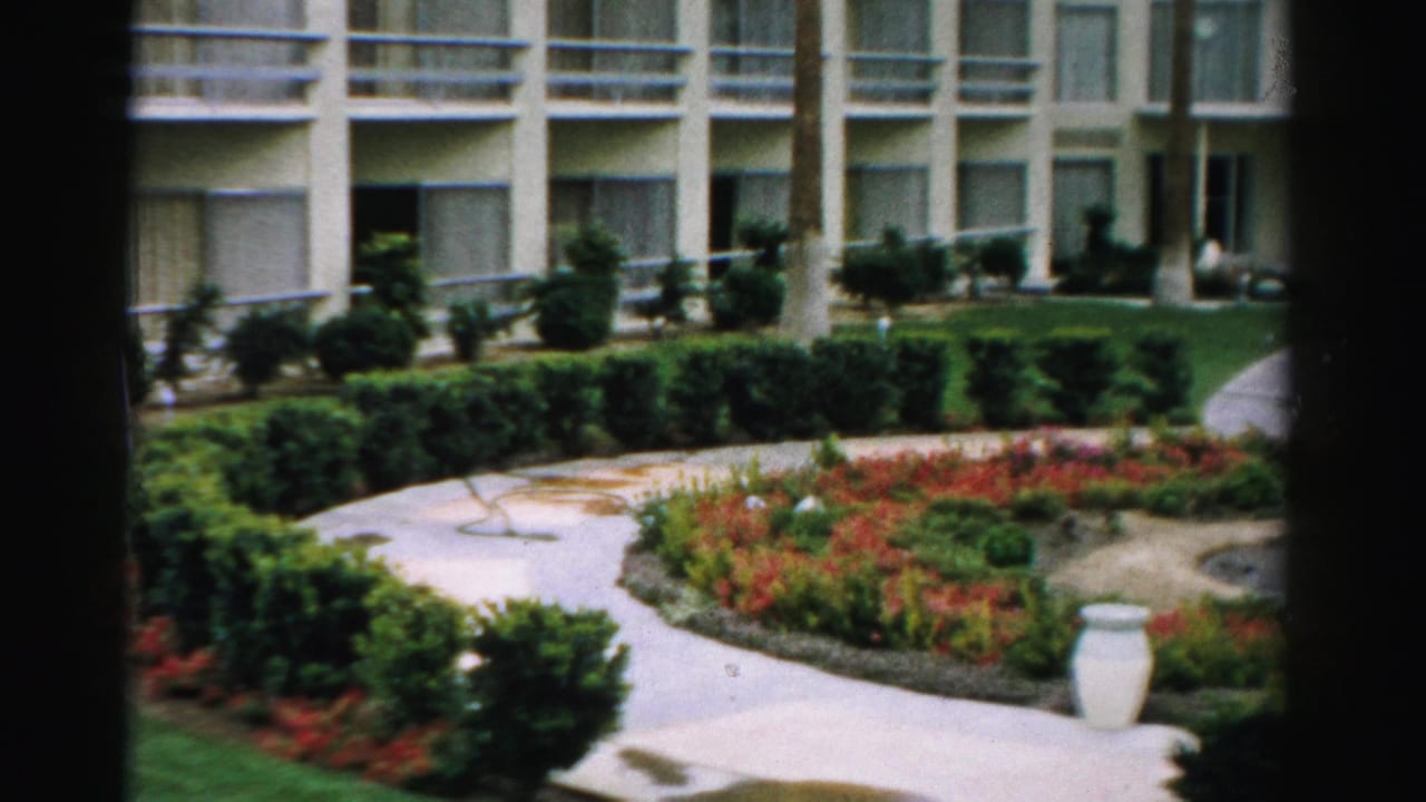 Apartment building and landscaped garden with curved path, hedges, flowers, urn, and fountain edge.