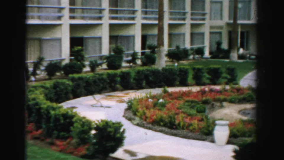 1957 Las Vegas apartment garden with balconies, trimmed hedges, red-orange flower beds, a curved walkway, white urn, and part of a circular fountain.