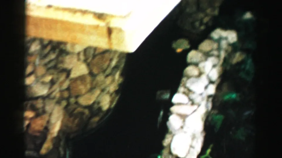 1957 Las Vegas frame showing a pale ledge, textured stone wall, narrow dark water, and a light rock border at the edge of the pond.