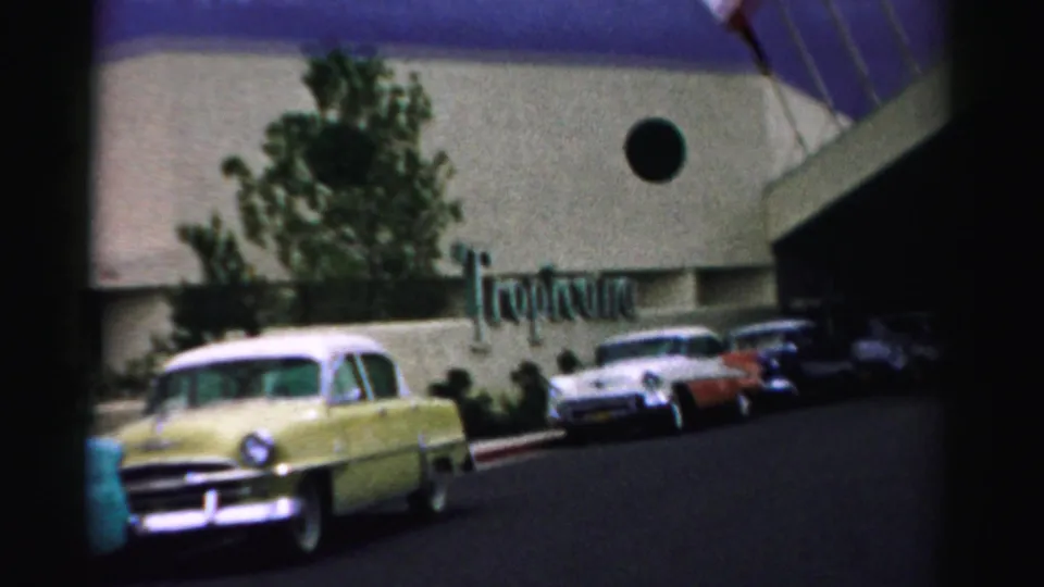 1957 Las Vegas home-movie frame showing a yellow two-tone sedan near the Tropicana sign and parked cars.