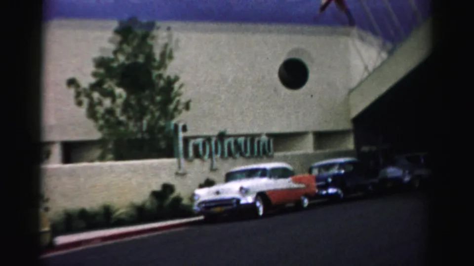 1957 Las Vegas frame showing the Tropicana sign, a white-and-red car, darker cars, and the hotel exterior.