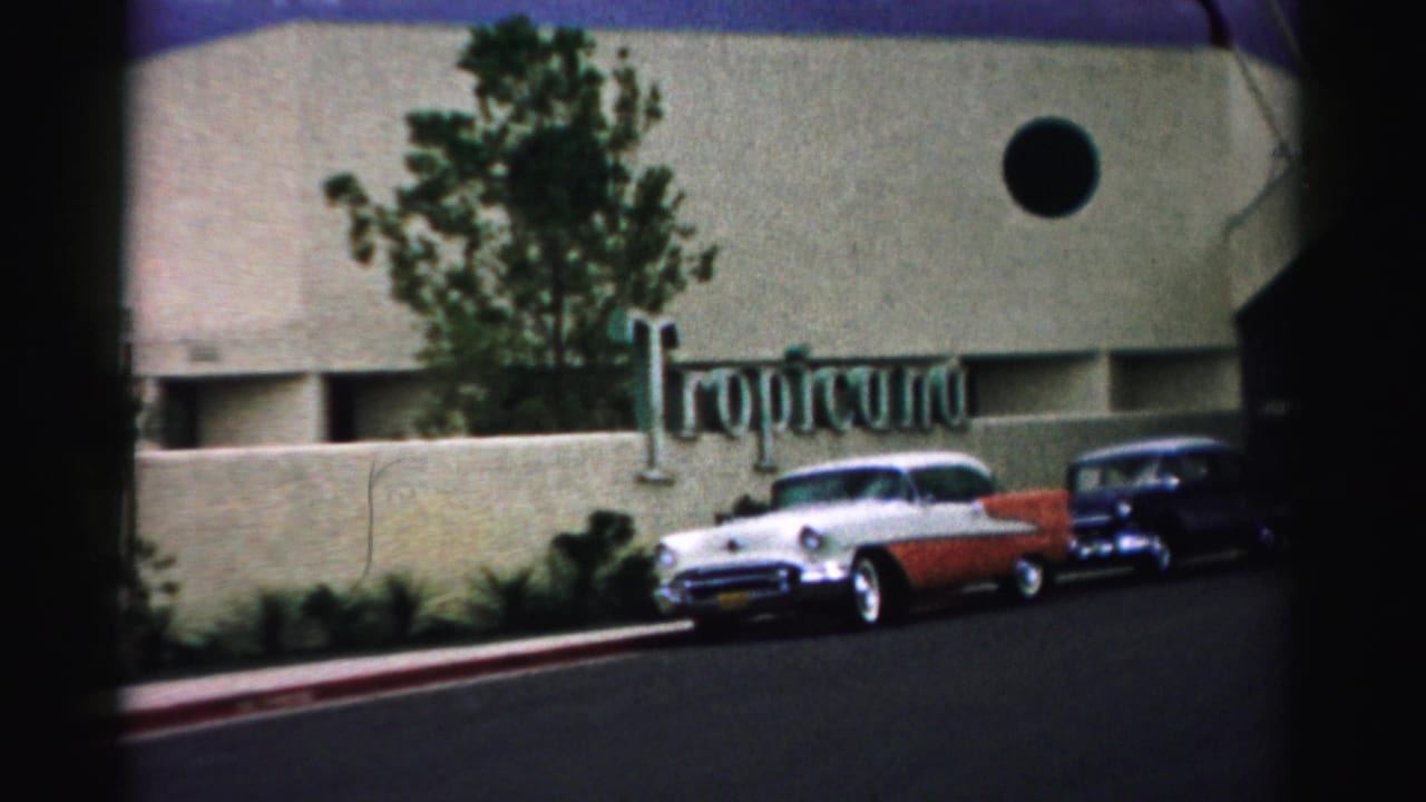 1957 Las Vegas home-movie view of the Tropicana frontage with a white and red 1950s sedan parked outside.