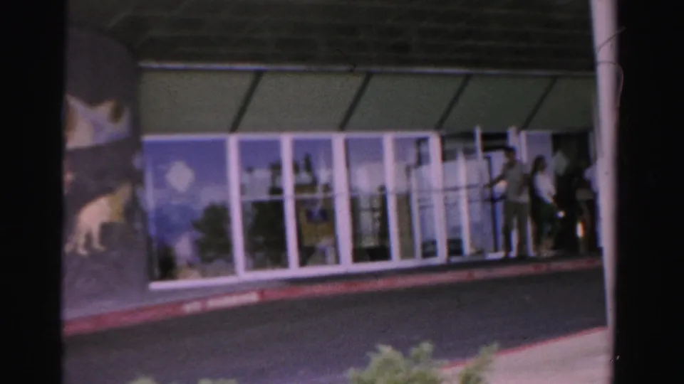 A few people stand near the Tropicana entrance area as the 8mm camera frames the glass doors from across the street.