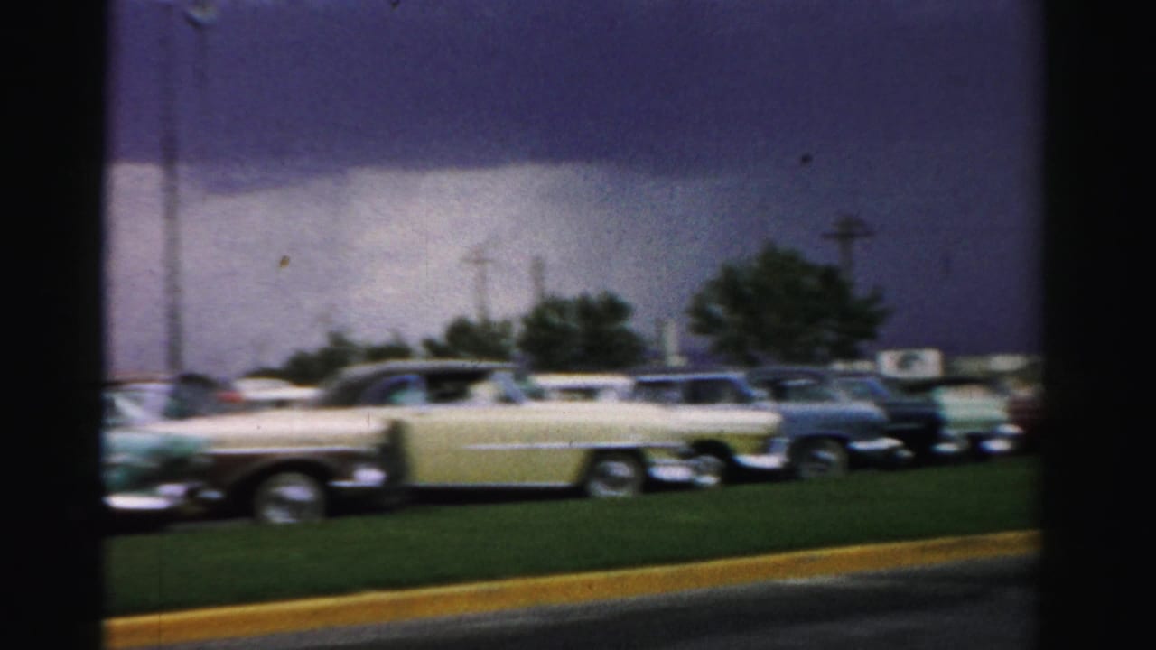 Parking area with several classic cars lined beside grass under a bright sky.
