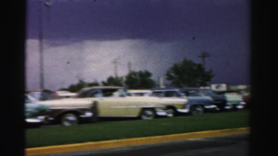 1957 Las Vegas church parking area with several mid-century cars, including a pale yellow vehicle, beside lawn and trees.