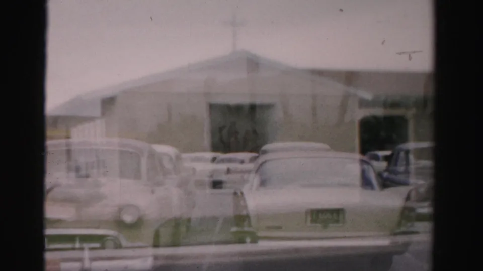 1957 Las Vegas street view with a beige church-like building, roof cross, and parked mid-century cars in soft 8mm color.