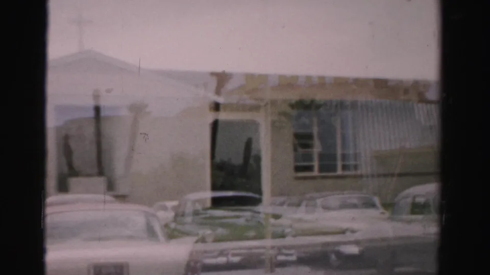 1957 Las Vegas home-movie frame showing a beige building facade, dark doorway, windows, and parked mid-century cars.