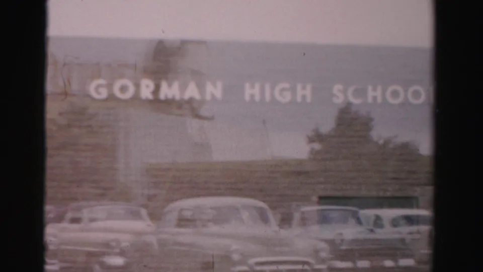 1957 Las Vegas home-movie view of the Gorman High School exterior, white lettering, and a row of parked cars.