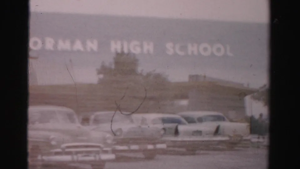 1957 Las Vegas frame showing the Gorman High School sign across the facade, with mid-century cars in the foreground.