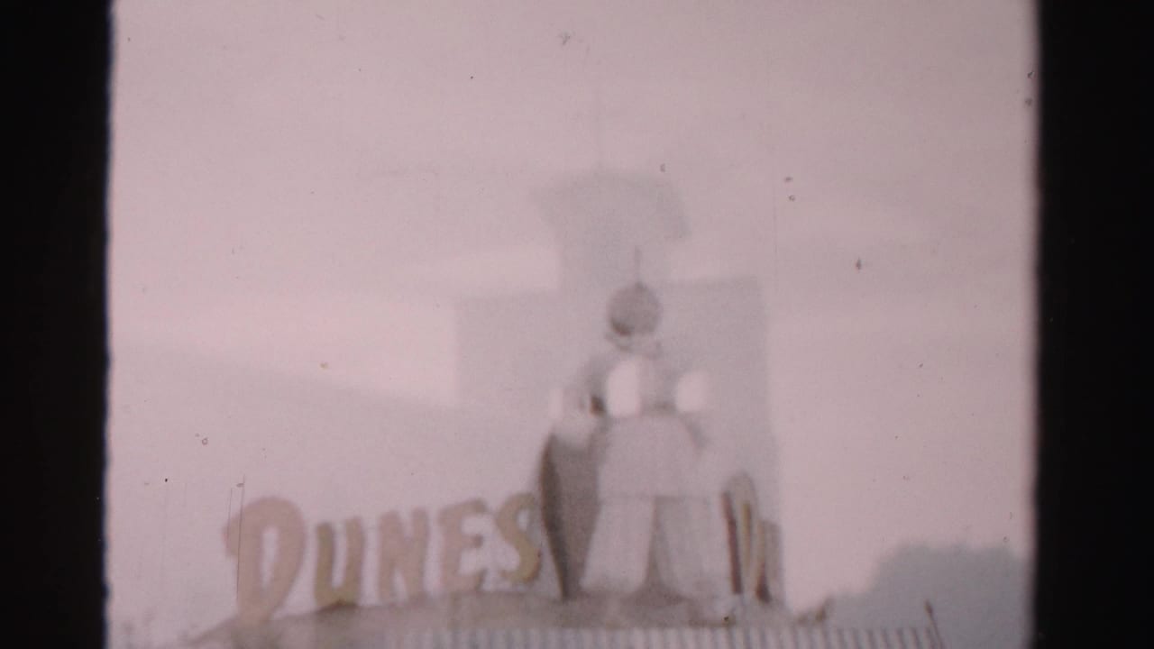 Dunes sign with a rooftop figure seen through a soft, faded 8mm frame.