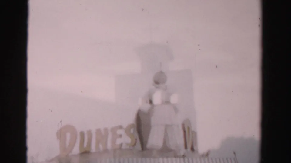 1957 Las Vegas home-movie frame showing Dunes lettering and a large rooftop figure in soft focus.