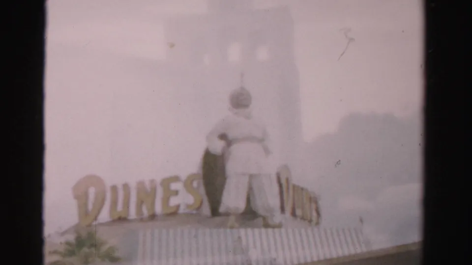 1957 Las Vegas frame with Dunes lettering, a large rooftop figure, roofline detail, and faded 8mm color.