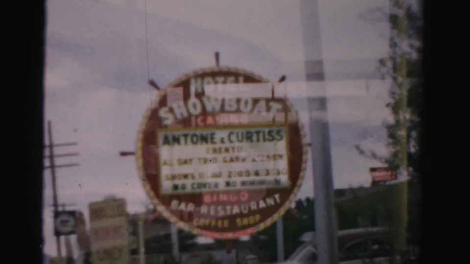1957 Las Vegas Hotel Showboat Casino marquee viewed through a window, with blurred show listings and roadside structures behind it.