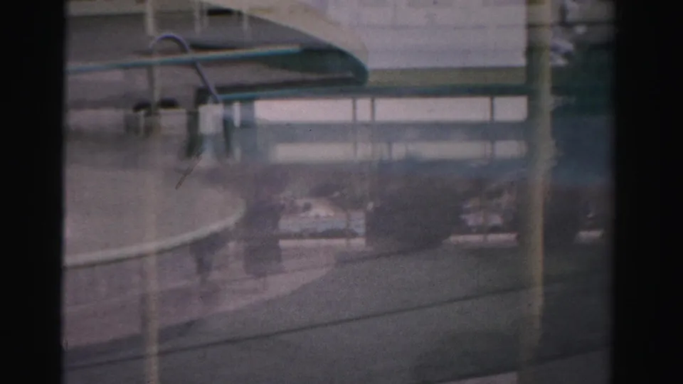 A low, soft 8mm view through glass in Las Vegas shows a vehicle side, street surface, reflections, and faint background structures.