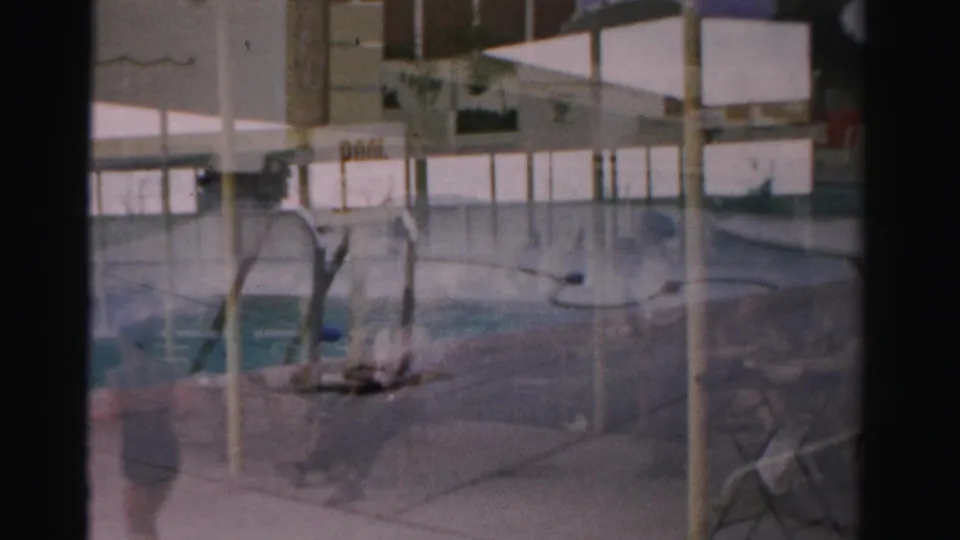 1957 Las Vegas home-movie view across a resort pool deck, with a ladder, closed sign, seating, and distant blurred people.